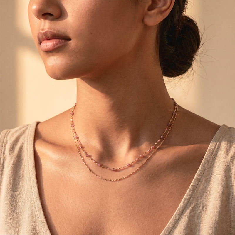 Woman wearing a layered pink tourmaline and gold chain necklace in warm daylight