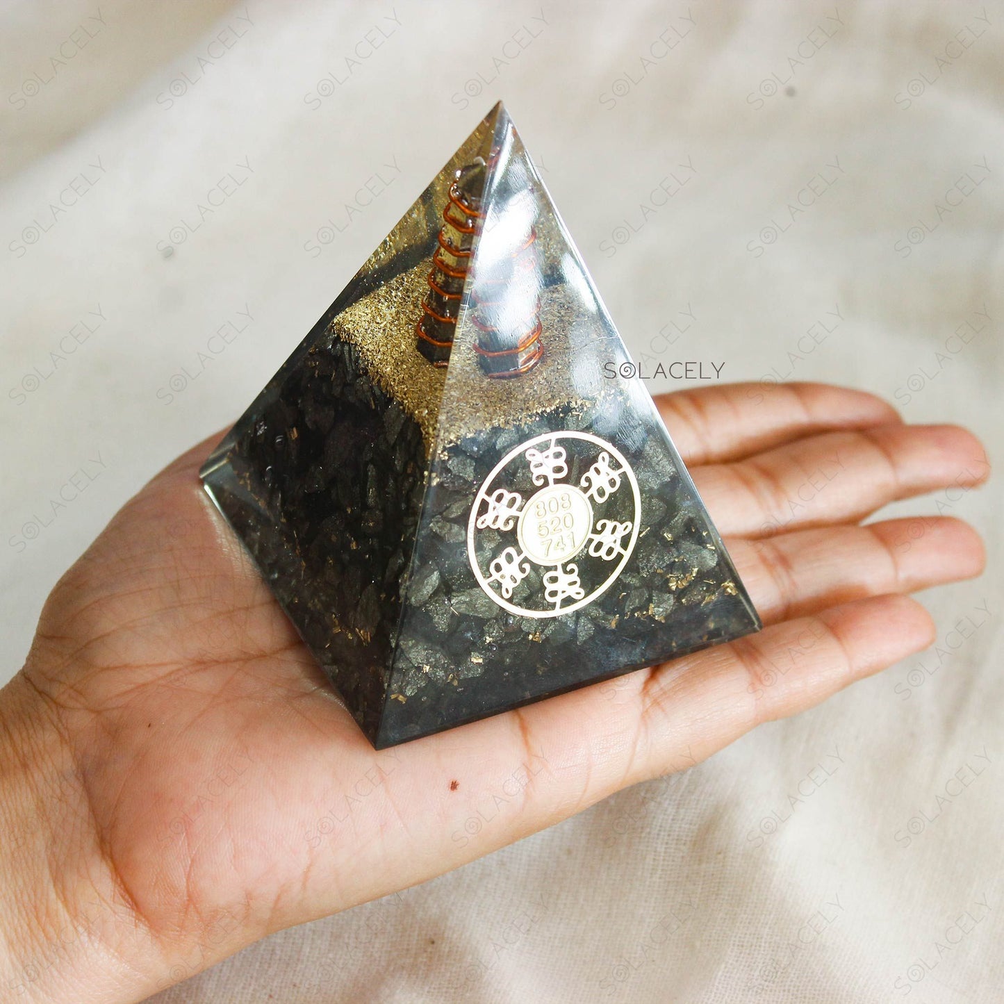 Hand holding a black and gold orgone pyramid with pyrite