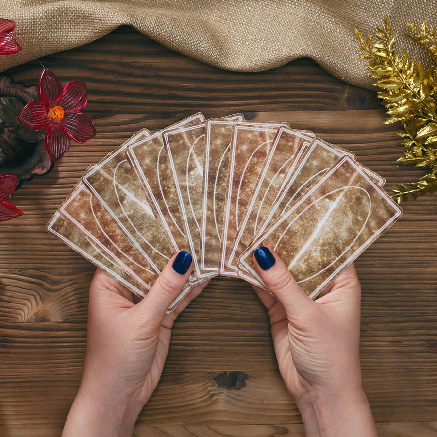 Hands holding brown tarot cards on wooden table.