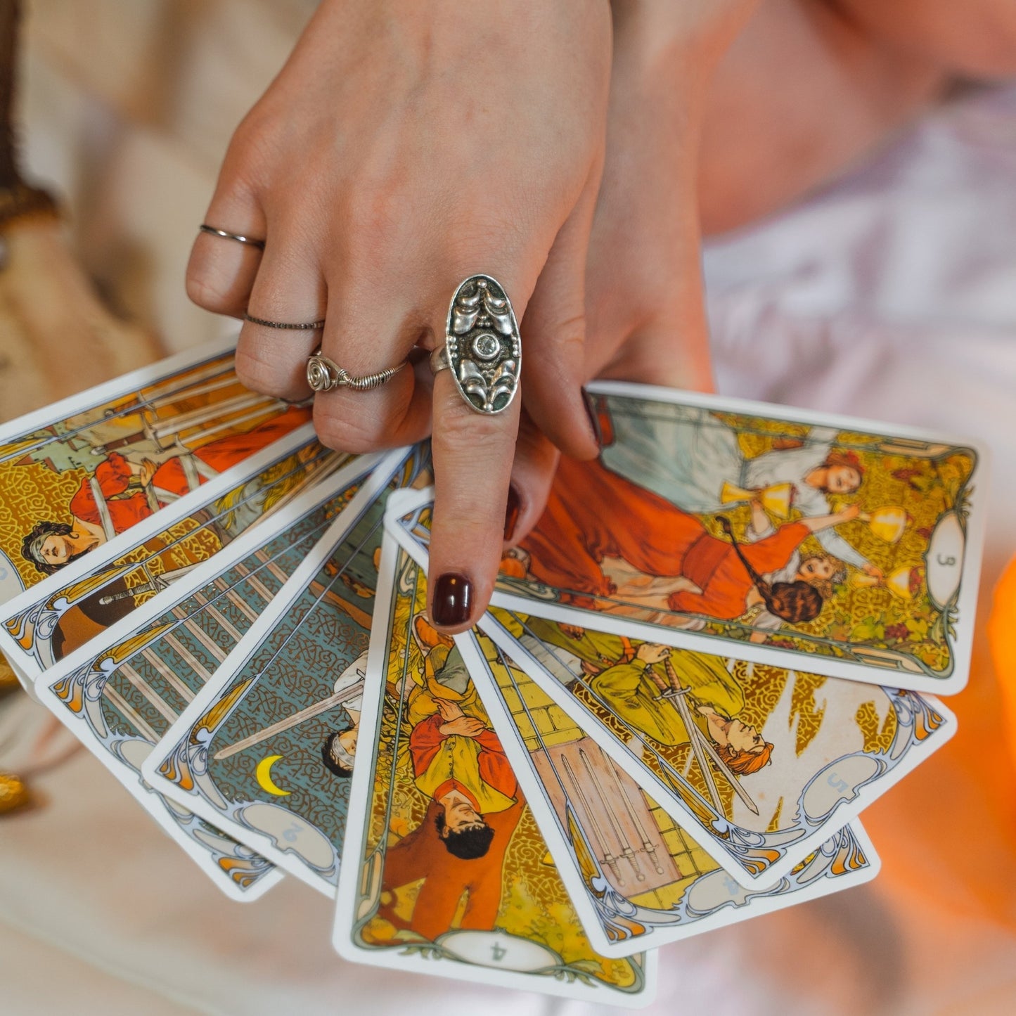 Hand with silver rings holding colorful tarot cards.