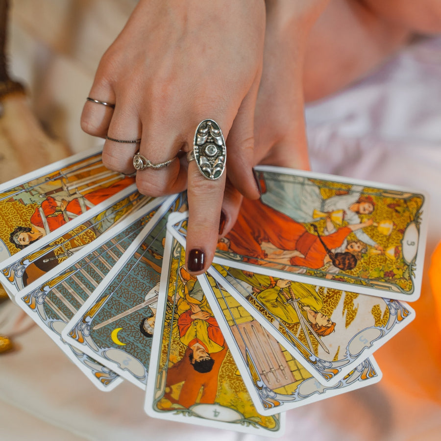 Hand with silver rings holding colorful tarot cards.