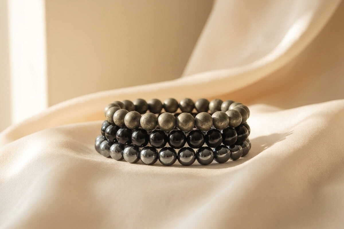 Stacked protection bead bracelets in pyrite, black obsidian and hematite on cream silk