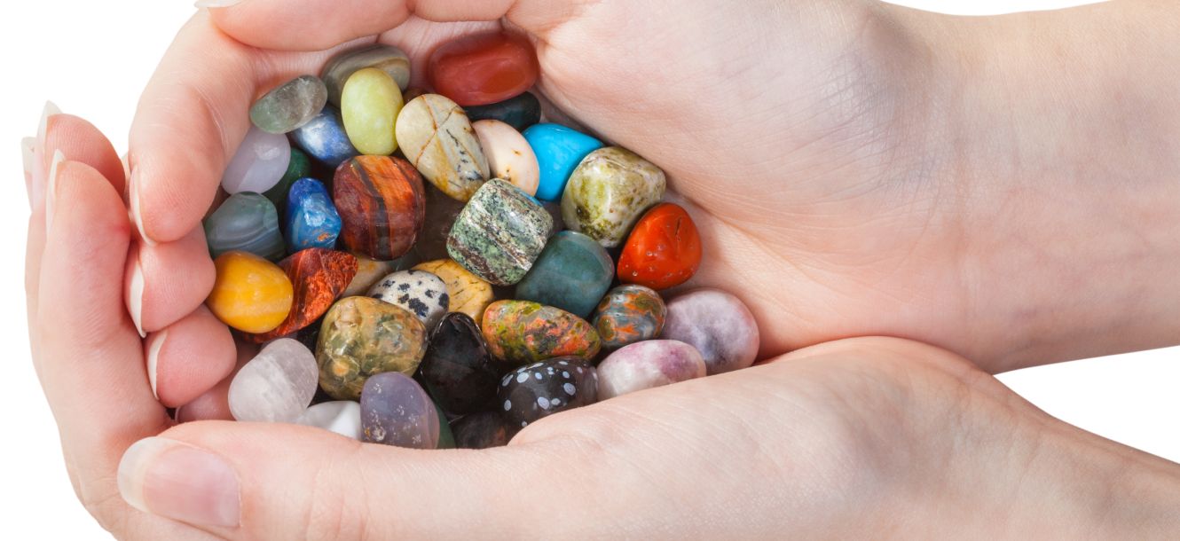 Two cupped hands holding a colourful pile of tumbled healing stones