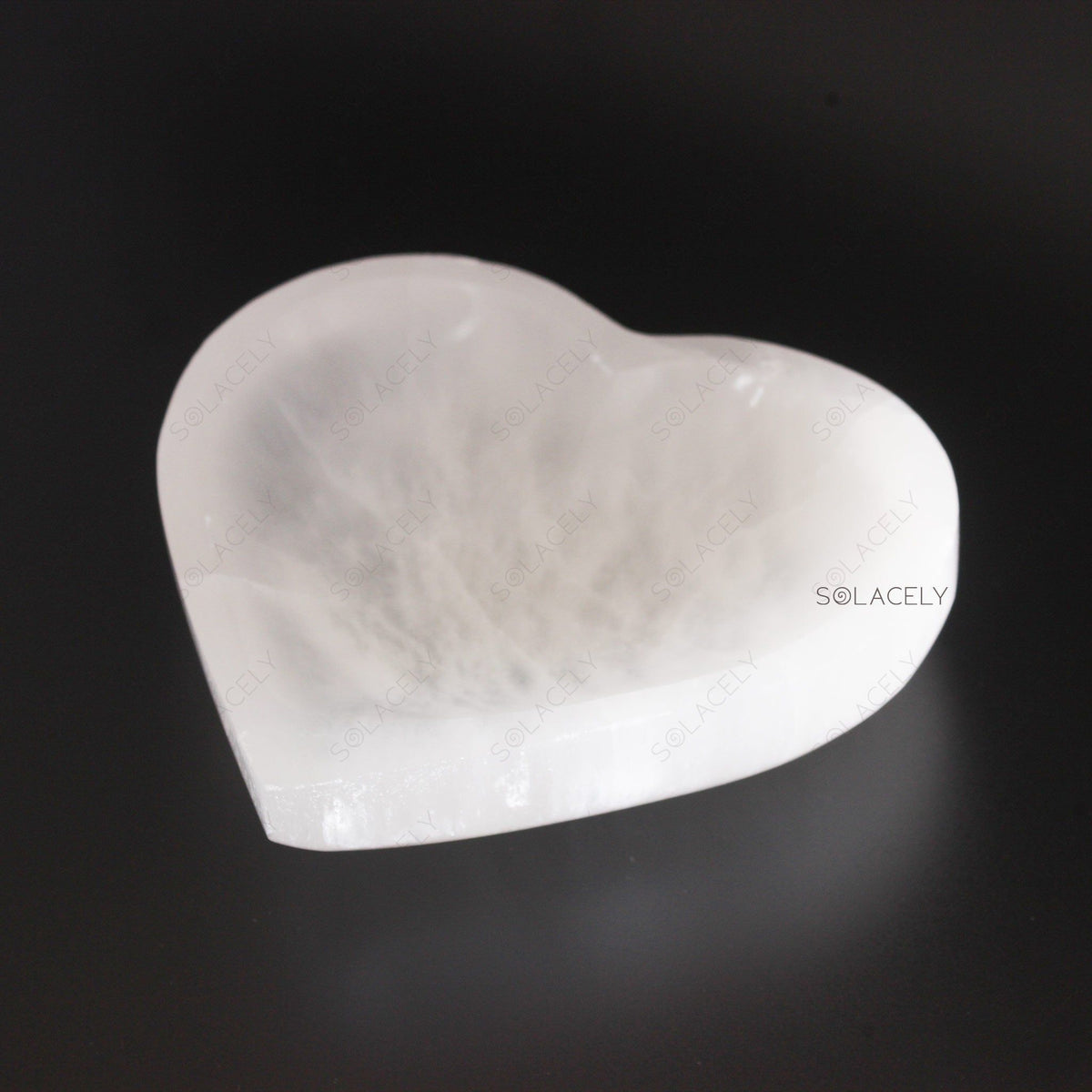 Polished white selenite heart stone on black background