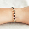 Hand wearing black, peach, and clear gemstone bracelet.