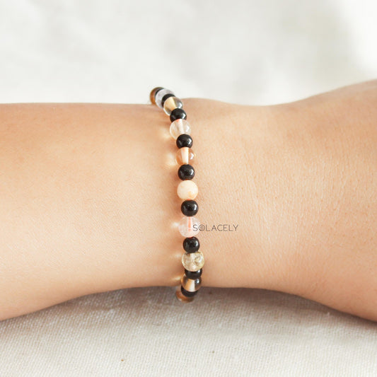 Hand wearing black, peach, and clear gemstone bracelet.