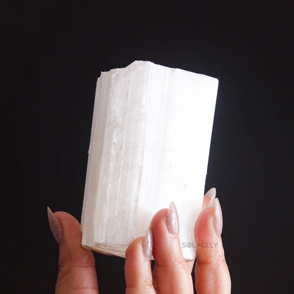 White Selenite crystal held against a dark background.