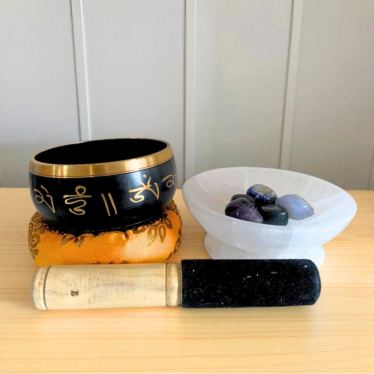 Selenite charging bowl holding crystal tumbles beside a singing bowl and mallet