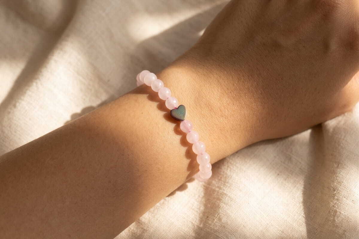 Rose quartz bead bracelet with a heart charm worn on a wrist in soft daylight