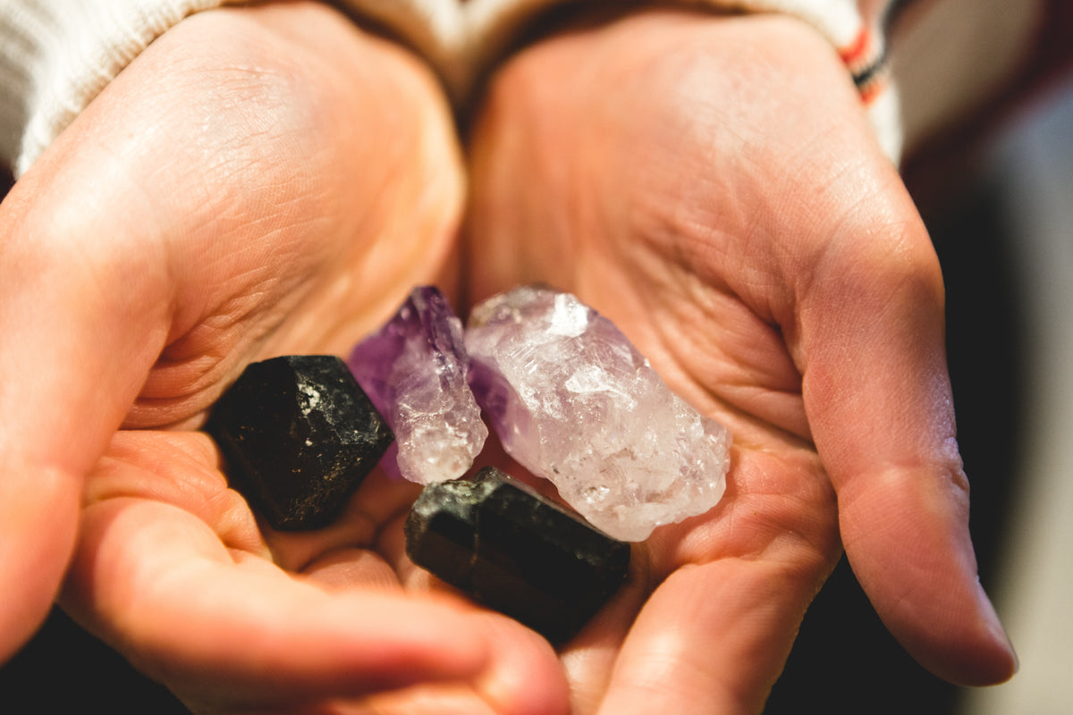 Cupped hands holding black tourmaline, amethyst and clear quartz stones
