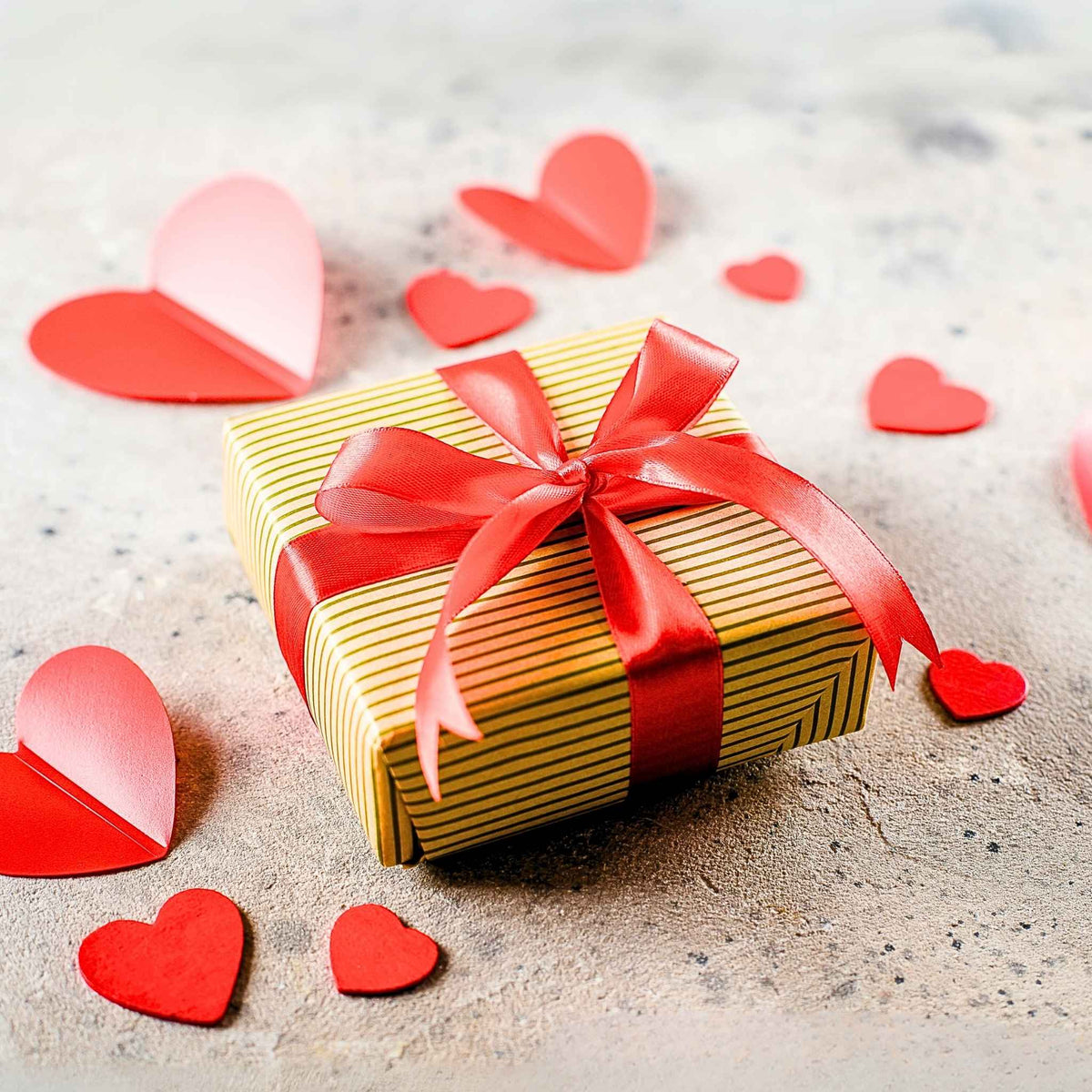 Valentine's gift box tied with a red ribbon, surrounded by paper hearts